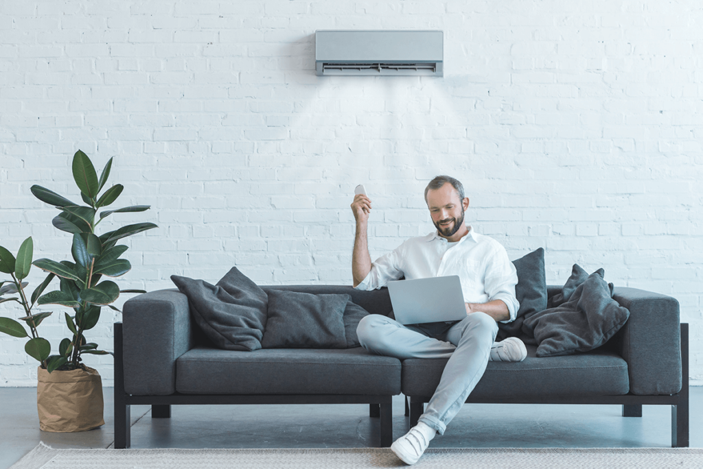 man smiling while holding a laptop and air conditioner remote