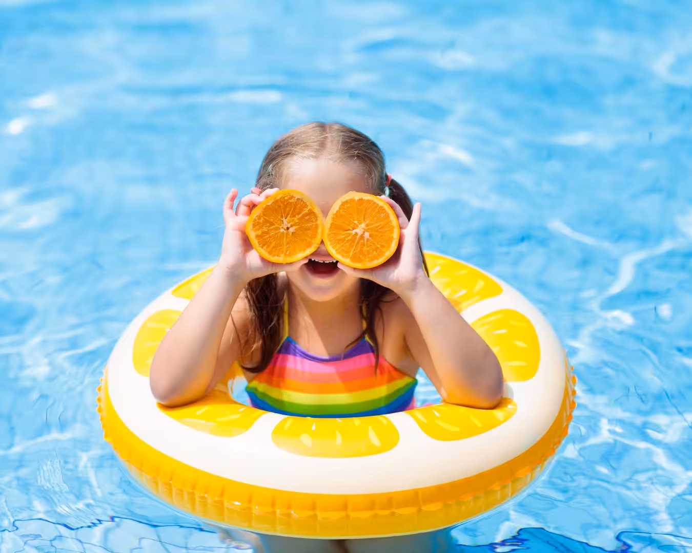A girl with oranges and floater in a pool