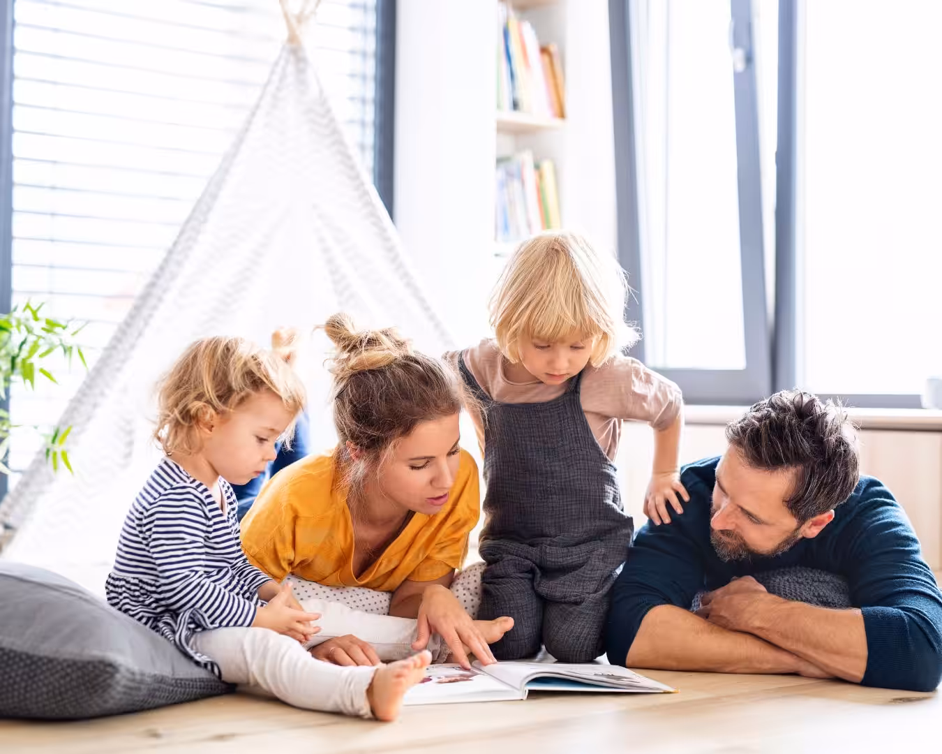 A family of four lying down while reading a book